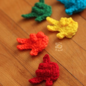 May include: A collection of colorful, crocheted hand-shaped items in red, yellow, green, and blue. The items are scattered on a wooden surface. The Etsy shop name "Crochet by Jayne" is visible in the image.