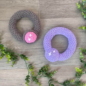 May include: Two crocheted rings with star-shaped embellishments. One ring is gray and the other is purple.