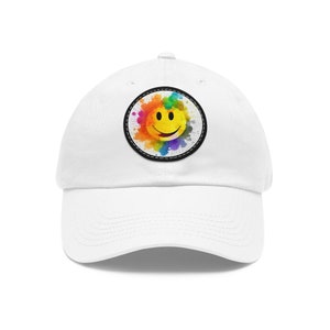 Puede incluir: Gorra de béisbol blanca con un parche de cara sonriente de colores. El parche tiene un efecto de acuarela arcoíris y un borde negro cosido.