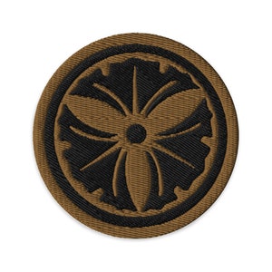 May include: A brown embroidered patch with a black stylized flower design. The flower has five petals and a center circle.