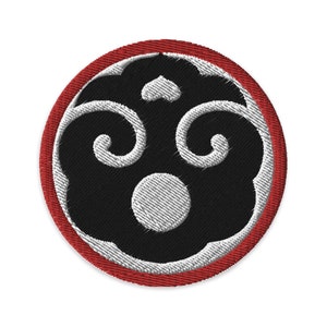 May include: A red and black embroidered patch with a stylized design of a circle with three swirls and a central circle. The patch has a red border.