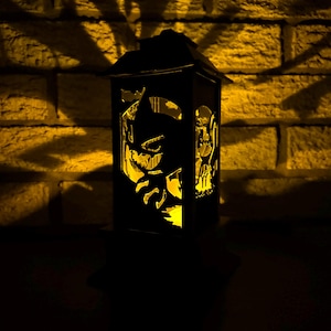 May include: A black lantern with a carved design of a skull and crossbones. The lantern is lit from within, casting a warm glow.