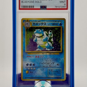 Może przedstawiać: Karta Pokemon Blastoise, niebieskiego Pokemona ż&oacute;łwia z pancerzem, oceniona przez PSA w ochronnym etui. Karta pochodzi z japońskiego podstawowego zestawu z 1996 roku i została oceniona na 9, co oznacza, że jest w idealnym stanie.