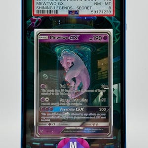 Może przedstawiać: Zklasyfikowana karta kolekcjonerska Pokemon z Mewtwo GX z zestawu Shining Legends. Karta jest w stanie prawie idealnym i ma ocenę PSA 8. Karta jest otoczona niebieskim i fioletowym etui ochronnym.