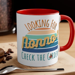 May include: White ceramic mug with a red rim and handle. The mug features a retro-style graphic with the text "Looking for Nonno? Check the Garden" and a small tomato plant illustration.