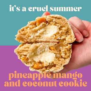Puede incluir: Primer plano de una galleta partida con un relleno blanco y trozos de piña y mango. La galleta está siendo sostenida por una mano y el texto "it's a cruel summer" está por encima de la galleta y el texto "pineapple mango and coconut cookie" está por debajo de la galleta.