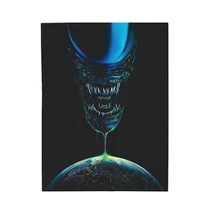 May include: A black blanket featuring a detailed illustration of an alien creature's head with sharp teeth, dripping onto a green and blue planet. The alien's head is primarily teal and blue, set against a dark background.