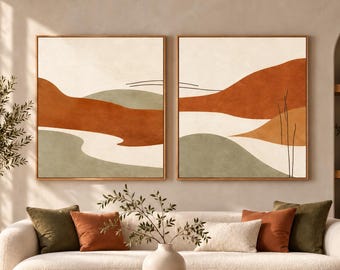 May include: Two square wall art pieces in wooden frames featuring abstract landscape designs. The artwork displays layered shapes in terracotta orange, sage green, and cream, accented by thin black line drawings of grass and horizon.