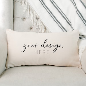 May include: A white throw pillow with the text "your design HERE" in black cursive font. The pillow is on a white couch with a white and black striped throw blanket.