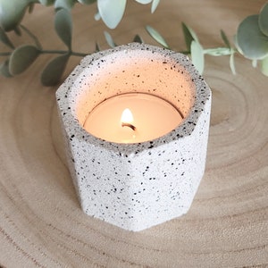 May include: A white, speckled, hexagonal candle holder with a lit tea light inside.