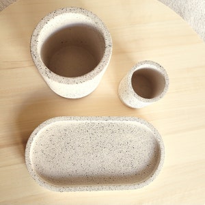 May include: Three speckled white ceramic containers: a large cylindrical vase, a smaller cylindrical vase, and an oval tray. The containers have a speckled white and black finish.