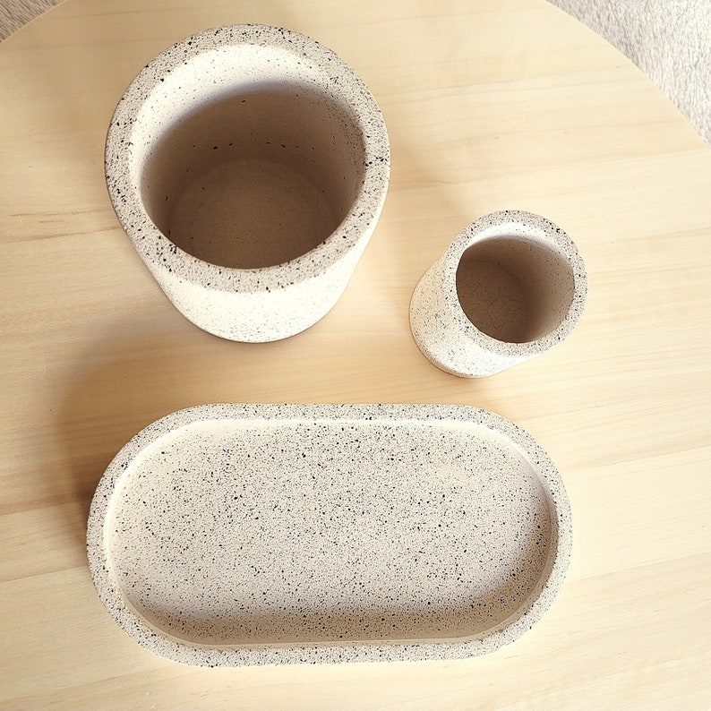May include: Three speckled white ceramic containers: a large cylindrical vase, a smaller cylindrical vase, and an oval tray. The containers have a speckled white and black finish.