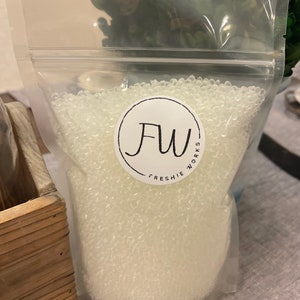 May include: A clear plastic bag filled with small, white, round beads. The bag has a white label with the text "FW Freshie Works" on it.