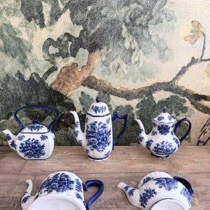 May include: Collection of white porcelain teapots with blue floral designs. The teapots vary in shape and size, with blue handles and lids. Some teapots are upright, while others are lying on their sides.
