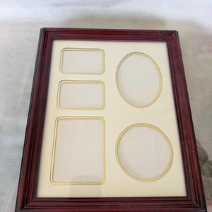May include: A rectangular picture frame with a dark cherry-colored wood finish and a cream-colored mat board. The mat features five openings: two small horizontal rectangles, one large vertical rectangle, one oval, and one circular opening.