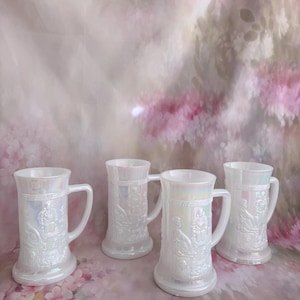 May include: Four iridescent white glass beer steins with handles. Each stein features a detailed embossed design of figures and architectural elements. The steins have a pearlescent finish, reflecting a range of colors.