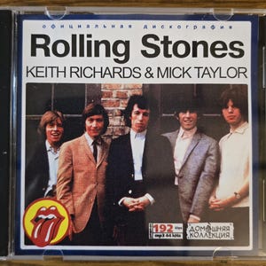 May include: A Rolling Stones music CD in a clear plastic case. The cover features a photograph of five band members, the text "Rolling Stones" and "KEITH RICHARDS & MICK TAYLOR," a red tongue logo, and technical audio specifications in Russian.