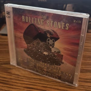 以下が含まれることがあります： ローリング・ストーンズのアルバム「Lost Treasures From The Brian Jones Era」のCDケース。カバーアートは、フィルムリールが入ったヴィンテージのチェストです。ケースは透明なプラスチック製で、2枚のCDが入っています。