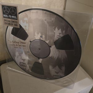 Peut inclure: Une bobine de bande magnétique en noir et blanc avec The Rolling Stones. L'étiquette indique une édition limitée spéciale et le texte "Live On Air 1965-1964 Volume One". La bobine est dans une pochette en plastique transparent.