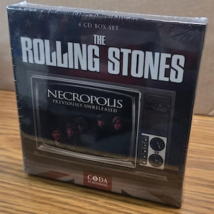 Könnte beinhalten: Versiegeltes 4-CD-Box-Set des Albums "Necropolis: Previously Unreleased" von "The Rolling Stones". Das Albumcover zeigt die Bandmitglieder in einem Vintage-Fernseher. Das Box-Set ist in Klarsichtfolie verpackt.