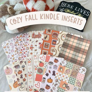May include: A collection of fall-themed Kindle inserts with various patterns, including pumpkins, leaves, and plaid designs. The text "COZY FALL KINDLE INSERTS" is displayed, along with "12 DESIGNS TO CHOOSE FROM" and "CLEAR CASE NOT INCLUDED". Two decorative pumpkin pillows are also visible.