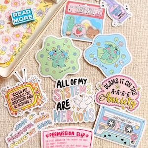 Puede incluir: Una colección de pegatinas coloridas con varios diseños y texto. Los diseños incluyen una rana, una cinta de cassette, un pulverizador y frases como "All of my systems are nervous" y "Permission Slip".