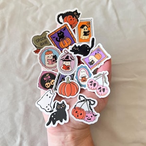 May include: A collection of Halloween-themed stickers featuring pumpkins, ghosts, black cats, and the text "Spook Babe." The stickers have a cartoon style with a variety of colors, including orange, black, purple, and pink.