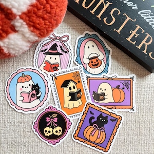 May include: A collection of Halloween-themed stickers featuring ghosts, pumpkins, and black cats. Each sticker has a unique design, including ghosts reading books and pumpkins with bats. The stickers are in various colors and framed with decorative borders.