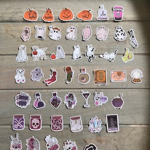 Peut inclure: Un ensemble de 36 autocollants sur le th&egrave;me d'Halloween avec des citrouilles, des fant&ocirc;mes, des chats, un chaudron de sorci&egrave;re, un cr&acirc;ne, une fiole de potion, un cristal, un squelette, un cercueil, et plus encore.