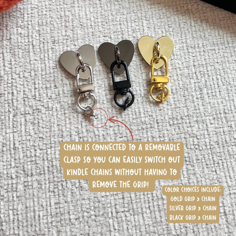 May include: Three heart-shaped keychain charms in silver, black, and gold. Each charm has a matching clasp and chain. Text on the image reads: "CHAIN IS CONNECTED TO A REMOVABLE CLASP SO YOU CAN EASILY SWITCH OUT KINDLE CHAINS WITHOUT HAVING TO REMOVE THE GRIP!"