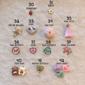 May include: A collection of romance charms, including a strawberry, daisy, hot air balloon, heart, pink puff, pink tassel, butterflies, teddy bears, and candy hearts. The charms are in various colors and designs, with the text "ROMANCE CHARMS" at the bottom.