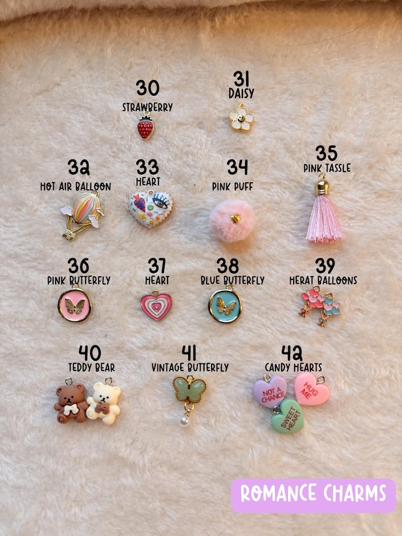 May include: A collection of romance charms, including a strawberry, daisy, hot air balloon, heart, pink puff, pink tassel, butterflies, teddy bears, and candy hearts. The charms are in various colors and designs, with the text "ROMANCE CHARMS" at the bottom.