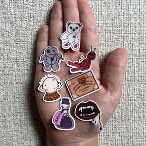 Peut inclure: Un ensemble de sept autocollants effrayants repr&eacute;sentant un ours en peluche blanc, une poup&eacute;e vaudou, une araign&eacute;e rouge, une boule de cristal, un planchette de ouija, une bouteille de poison et une bouche de vampire.
