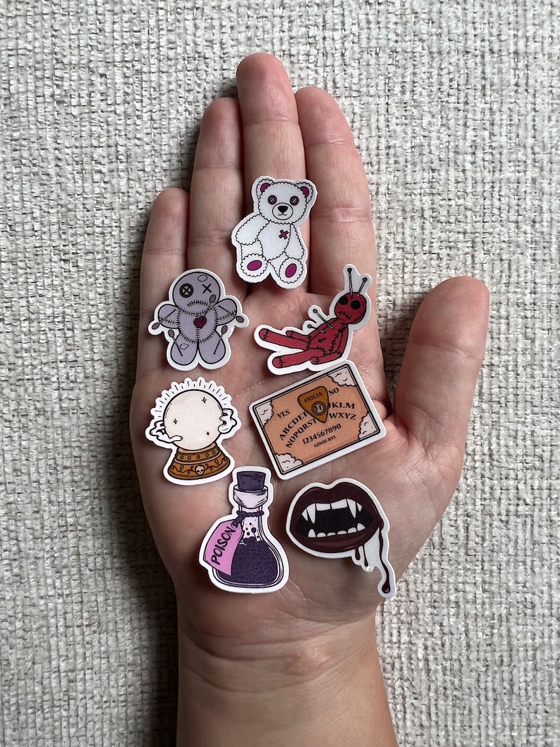 Peut inclure: Un ensemble de sept autocollants effrayants repr&eacute;sentant un ours en peluche blanc, une poup&eacute;e vaudou, une araign&eacute;e rouge, une boule de cristal, un planchette de ouija, une bouteille de poison et une bouche de vampire.
