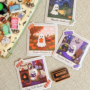 May include: A collection of four square stickers featuring ghost illustrations titled Monster Hunter, Pumpkin Patch Girlie, Haunted Reader, and Cozy Fall Reader, alongside a rectangular pin reading Bookish Halloween and a gold-toned charm bracelet.