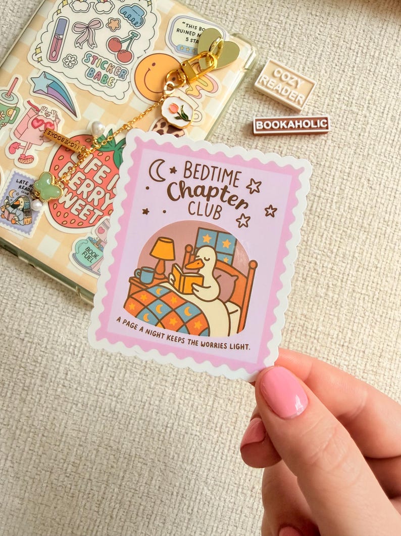 May include: A pink sticker with a scalloped edge shows a cartoon duck reading in bed under a crescent moon and stars. The sticker reads "Bedtime Chapter Club" and "A page a night keeps the worries light."