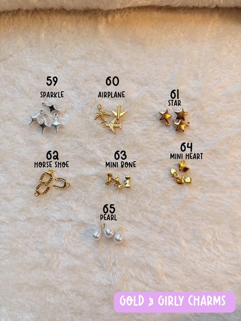 May include: An assortment of gold and silver charms, including stars, airplanes, hearts, and pearls, are displayed on a soft, white surface. The image includes text labels such as "SPARKLE," "AIRPLANE," and "PEARL." The text "GOLD & GIRLY CHARMS" is also visible.