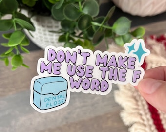 Op de afbeelding: Een sticker met een lichtblauw en paars ontwerp. De sticker zegt "Dwing me niet om het F-woord te gebruiken" en bevat een cartoonafbeelding van een flosdraaddoosje.