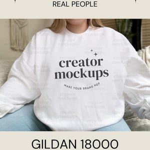 以下が含まれることがあります： 太字の「creator mockups」というテキストが入った白いGildan 18000スウェットシャツ。スウェットシャツはモックアップセットの一部で、上に「Real Backgrounds Real People」という言葉があります。
