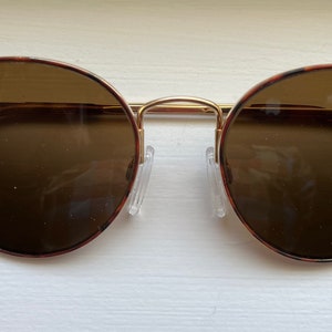 May include: Round brown tortoiseshell sunglasses with gold metal frames and brown lenses.