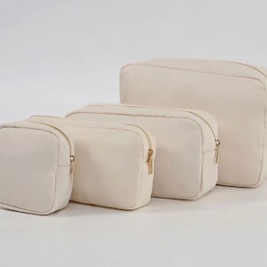 May include: Four off-white canvas zippered pouches of varying sizes. The pouches are lined up in a row from largest to smallest.