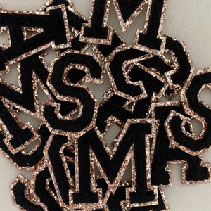 May include: A pile of black felt letters with a rose gold glitter outline. The letters are in various sizes and include the letters M, S, and R.