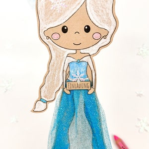 May include: A paper craft of a cartoon princess wearing a blue dress with a snowflake design. She is holding a sign that says "Einladung" which is German for "Invitation".