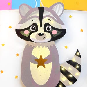 May include: A gray raccoon paper lantern with a black nose and eyes, a gold star, and a striped tail. The lantern has a white string for hanging and is decorated with small yellow stars.