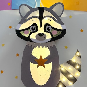 May include: A gray raccoon paper lantern with a white string for hanging. The raccoon is holding a gold star and has a striped tail with lights. The lantern is surrounded by yellow stars and brown leaves on a white background.