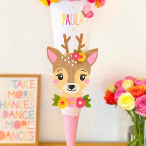 Könnte beinhalten: Ein rosa-weißer Schultüte, verziert mit einem Hirschgesicht, Blumen und dem Namen "PAULA".