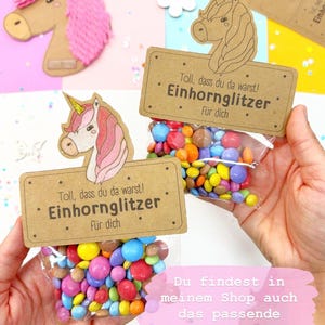 Puede incluir: Dos peque&ntilde;as bolsas de caramelos de colores con una etiqueta con tem&aacute;tica de unicornio que dice "Toll, dass du da warst! Einhornglitzer f&uuml;r dich". La etiqueta es marr&oacute;n con texto blanco y una ilustraci&oacute;n de unicornio.