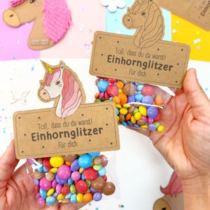 May include: Two small brown paper bags with unicorn illustrations and the text "Toll, dass du da warst! Einhornglitzer F&uuml;r dich" filled with colorful candy.
