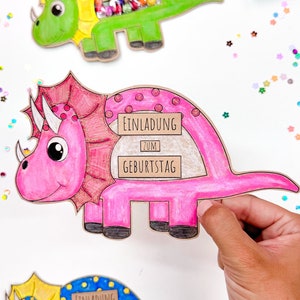 Pu&ograve; includere: Tre inviti colorati a forma di dinosauro con una finestra ritagliata per le leccornie. Gli inviti dicono "Einladung zum Geburtstag", che si traduce in "Invito al compleanno".