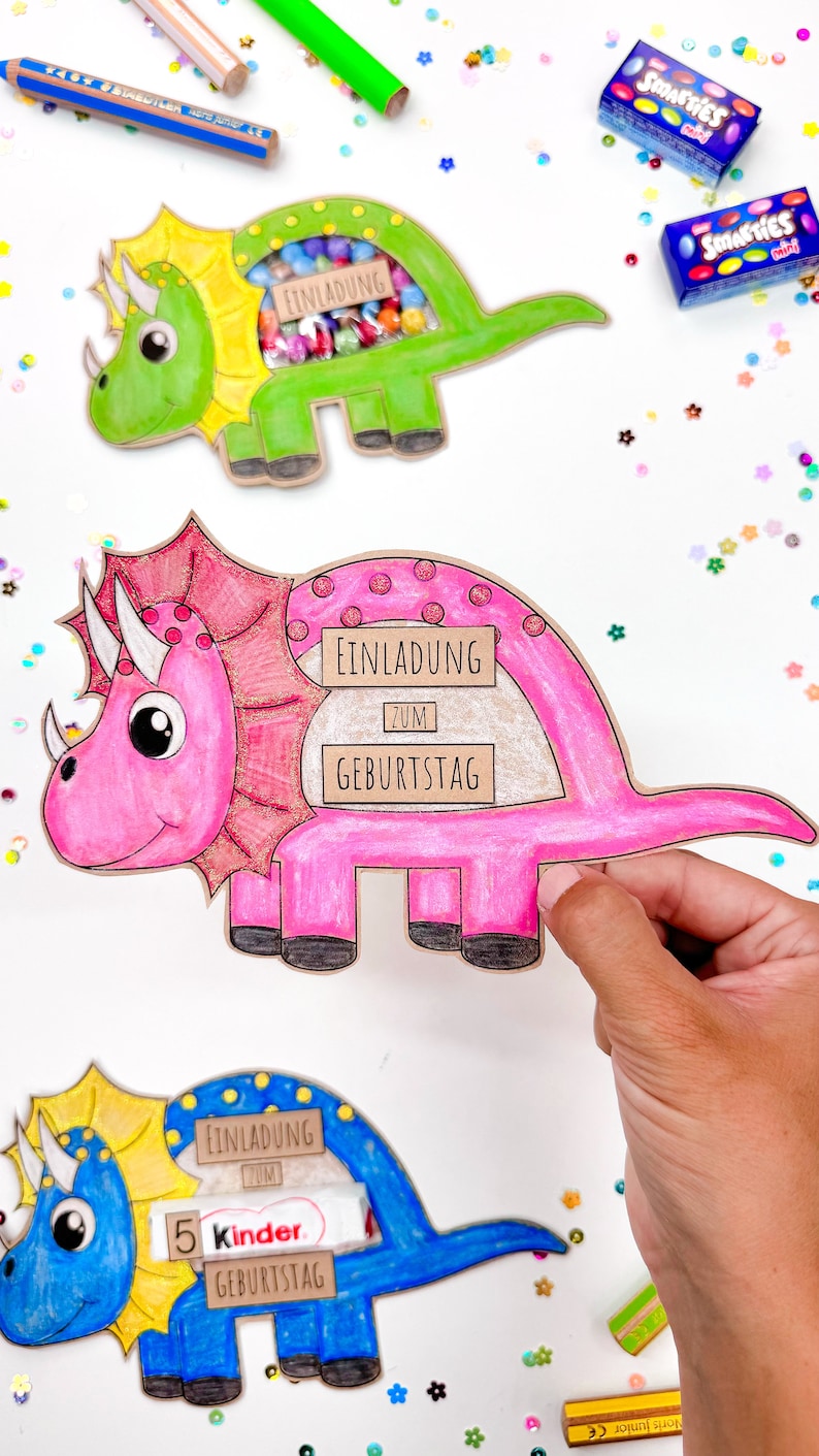 Pu&ograve; includere: Tre inviti colorati a forma di dinosauro con una finestra ritagliata per le leccornie. Gli inviti dicono "Einladung zum Geburtstag", che si traduce in "Invito al compleanno".
